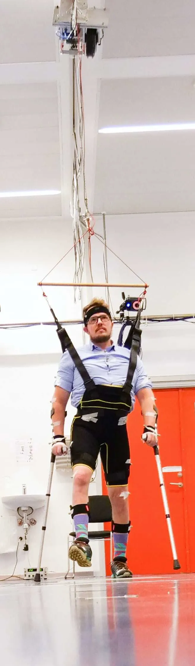 Jonas walking with crutches while RoboTrainer's ceiling rail carries part of his body weight